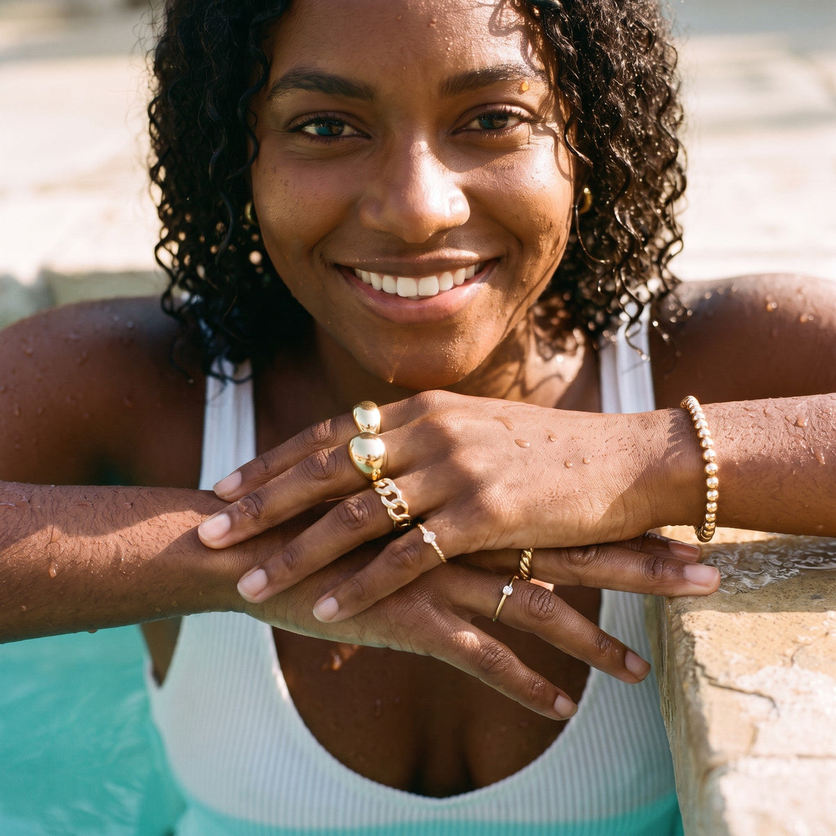Woman at the edge of a pool wearing stacked gold rings