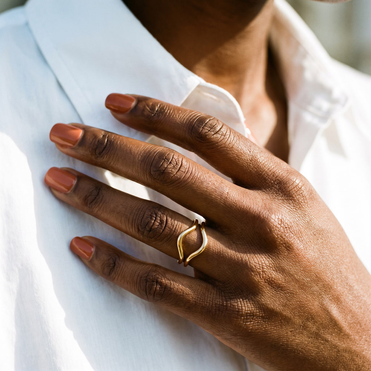 Hand wearing the gold Isla Wave Ring against a white shirt