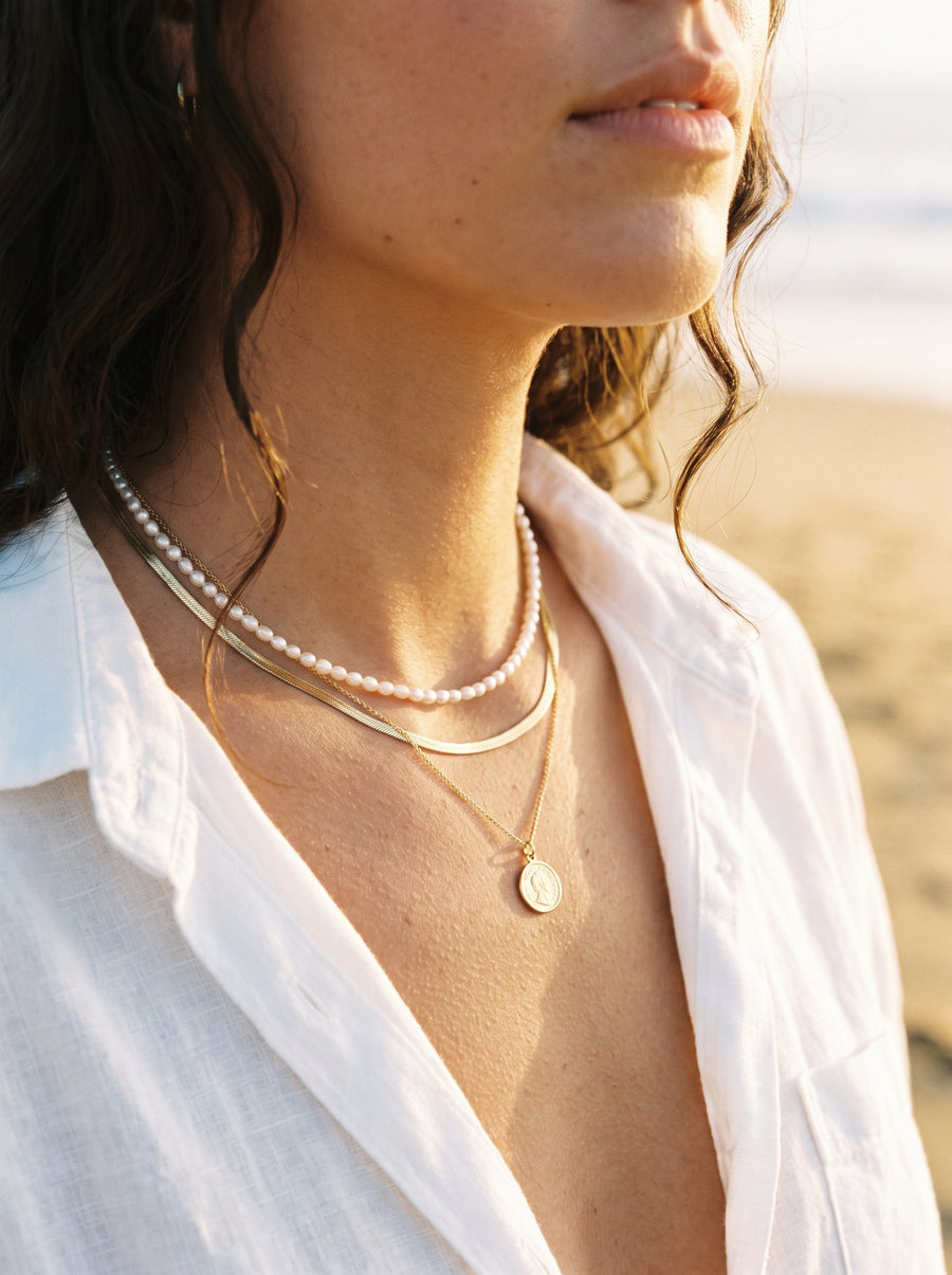 Layered gold necklaces with a pearl choker on a woman's neckline at the beach