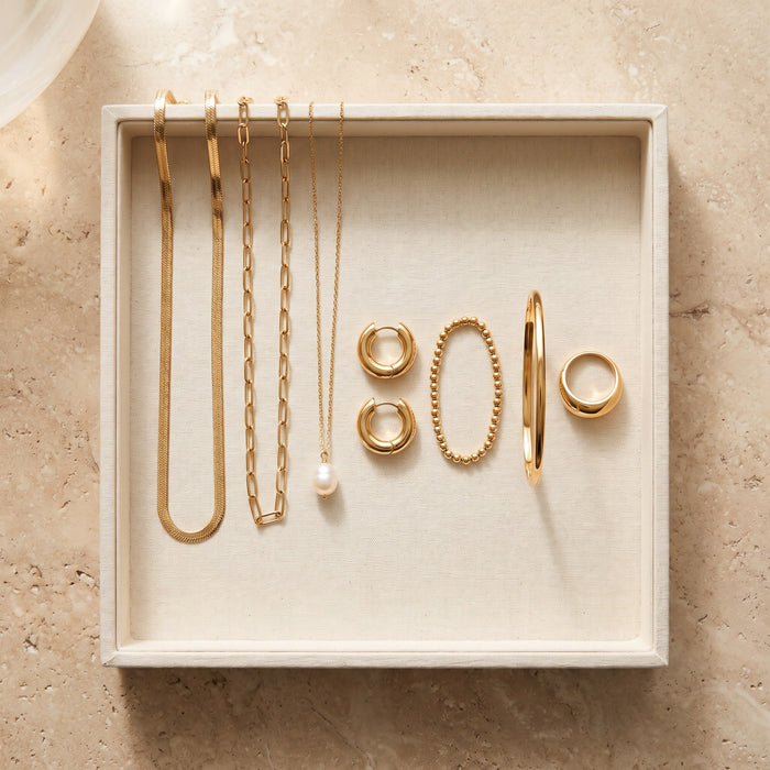 Seven gold jewelry pieces arranged in a cream jewelry tray