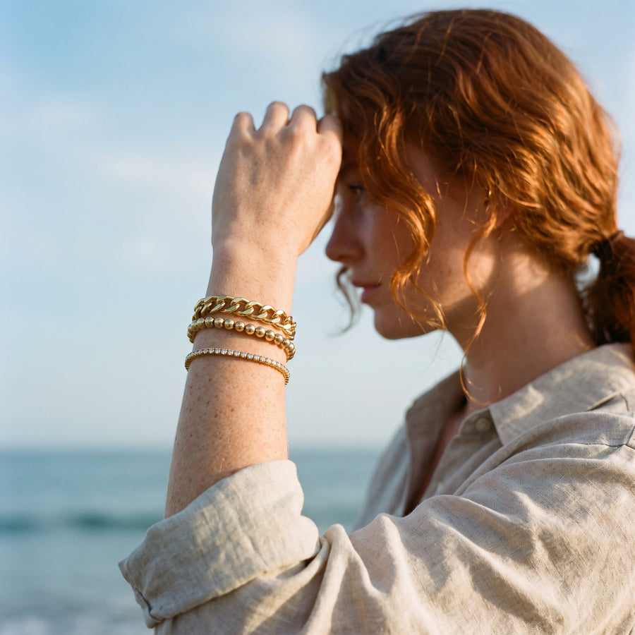 Red-haired woman shading her eyes, wearing a stack of gold bracelets