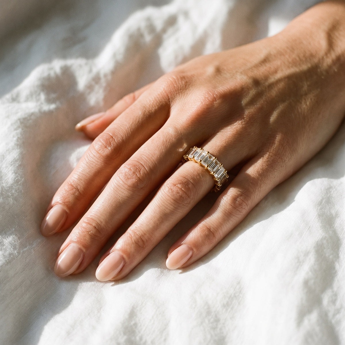 Hand wearing the gold Chiara Eternity Ring on white linen