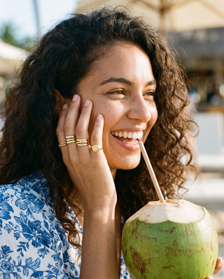 Woman with curly hair holding a coconut, wearing stacked gold rings